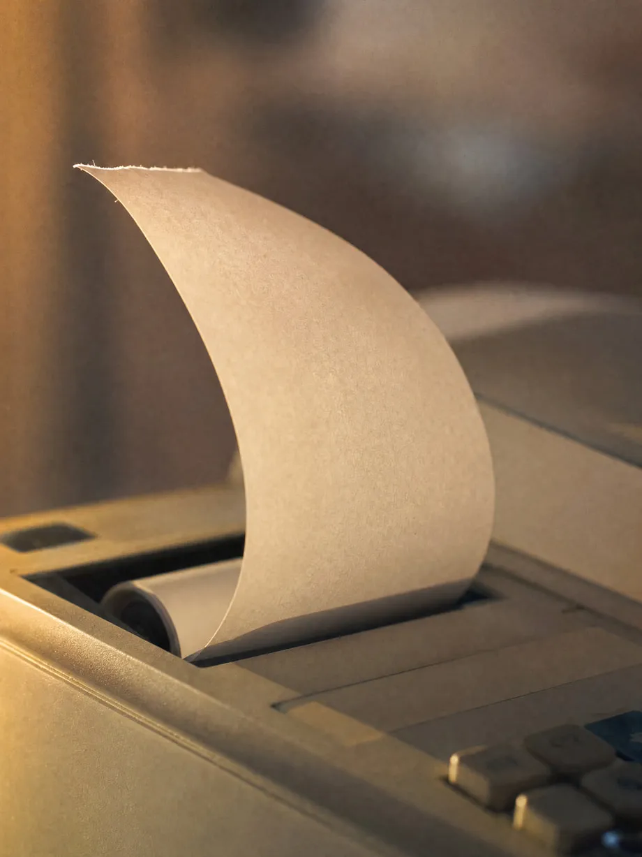 A folded receipt curling gently in warm light, mid-print.