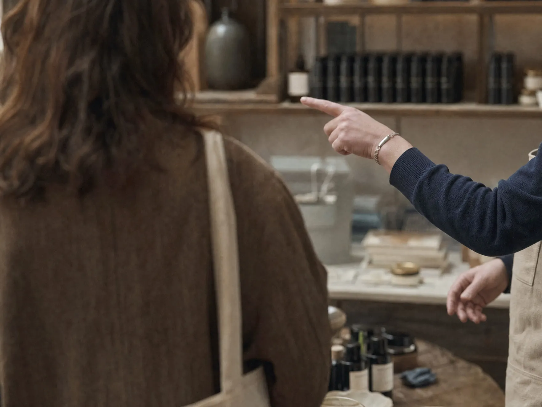 A retail associate's hand gesturing helpfully while a customer, seen from behind, listens.