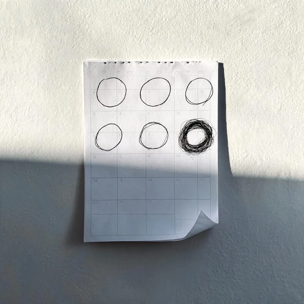 A paper September wall calendar in low light with six dates hand-circled in ink and one gone over repeatedly, representing next month’s scheduled developments to watch.
