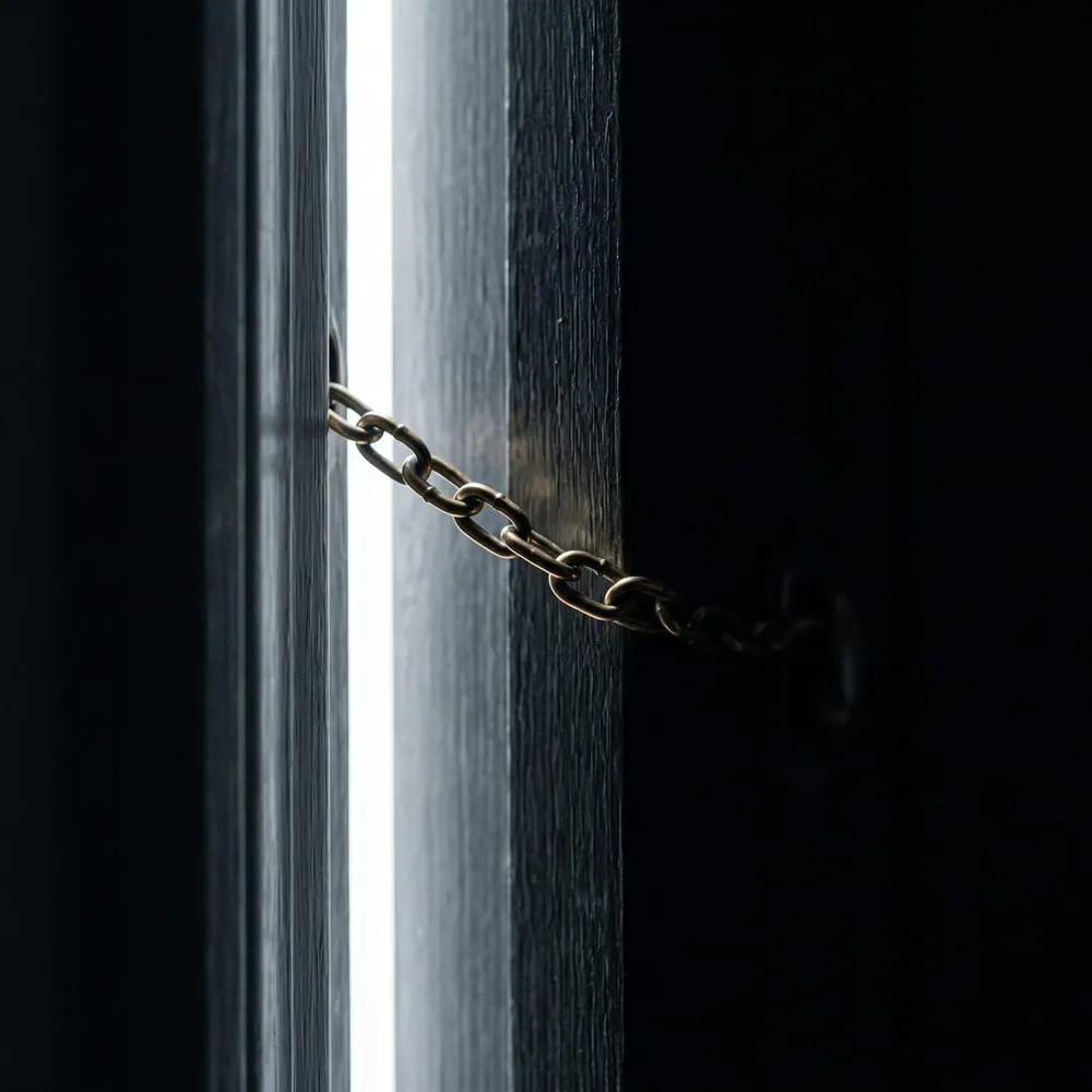 A taut brass door chain stretched across a narrow gap of light, illustrating Amazon blocking Meta's Muse shopping agent from Amazon.com under its terms of use.