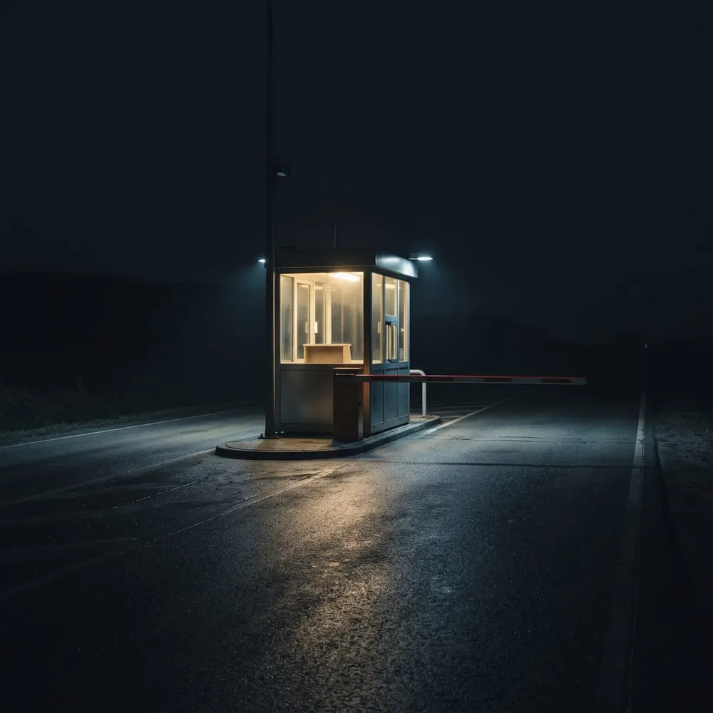 An unattended tollbooth at night with its barrier down on an empty road, illustrating the view that card networks intend to charge merchants for verifying AI agents.